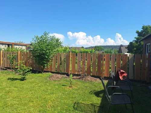 Ein frisch aufgestellter Zaun aus naturbelassenen Planken mit Rindenkanten und viel Abstand zwischen den einzelnen Brettern. Inspiriert von Weidezäunen.