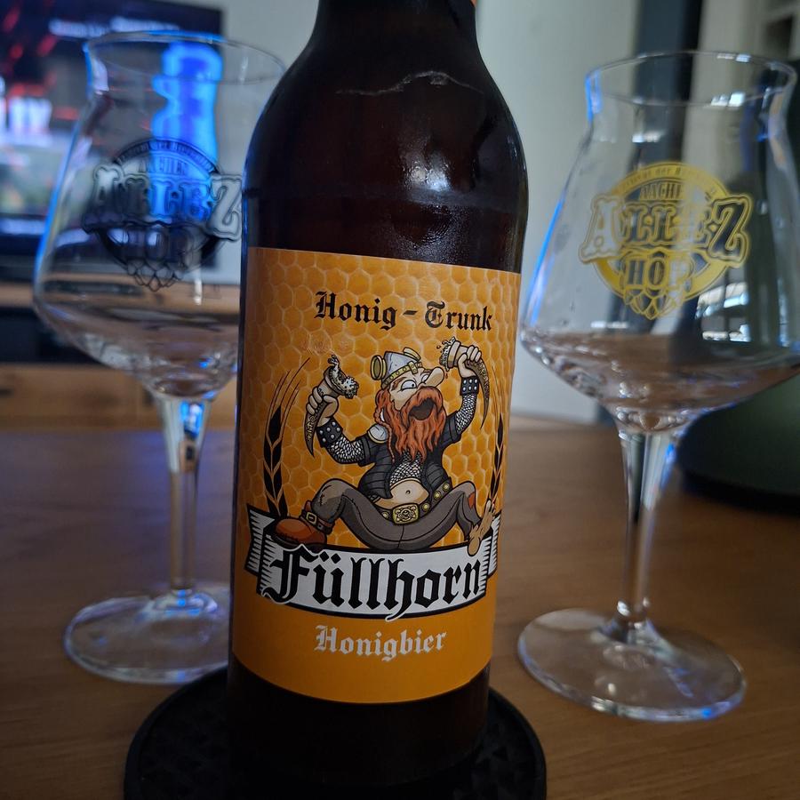 Ein Foto von einer Flasche "Füllhorn" Honigbier. Im Hintergrund daneben, zwei Tastinggläser vom Allez Hop Bierfestival.