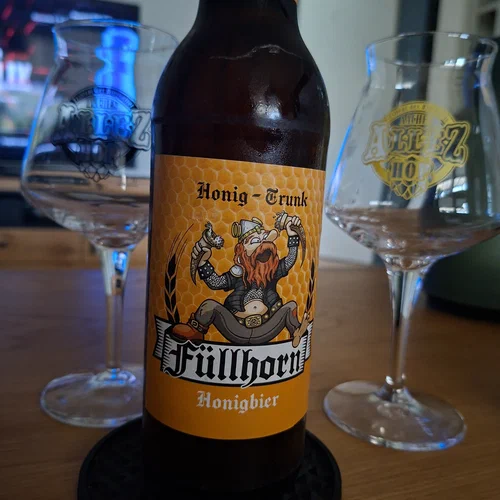 Ein Foto von einer Flasche "Füllhorn" Honigbier. Im Hintergrund daneben, zwei Tastinggläser vom Allez Hop Bierfestival.