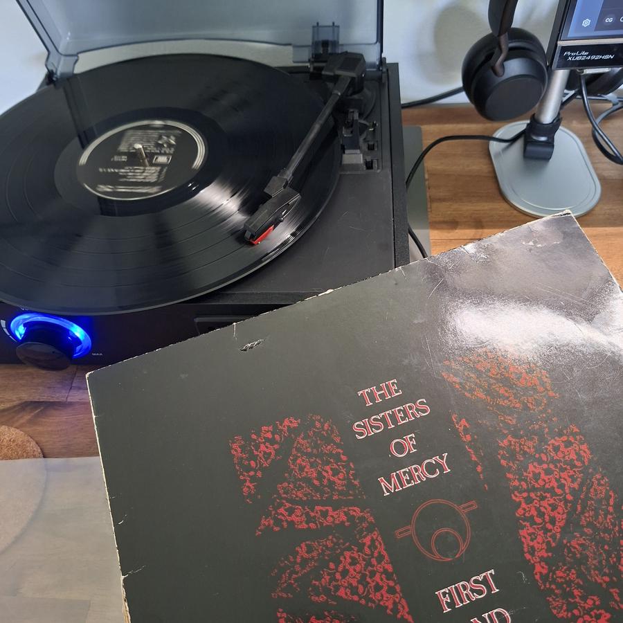 Ein Foto von einem Schallplatten-Spieler, auf dem eine schwarze Vinyl-LP liegt. Davor angelehnt ist das Cover: Sisters Of Mercy, First and Last and Always.